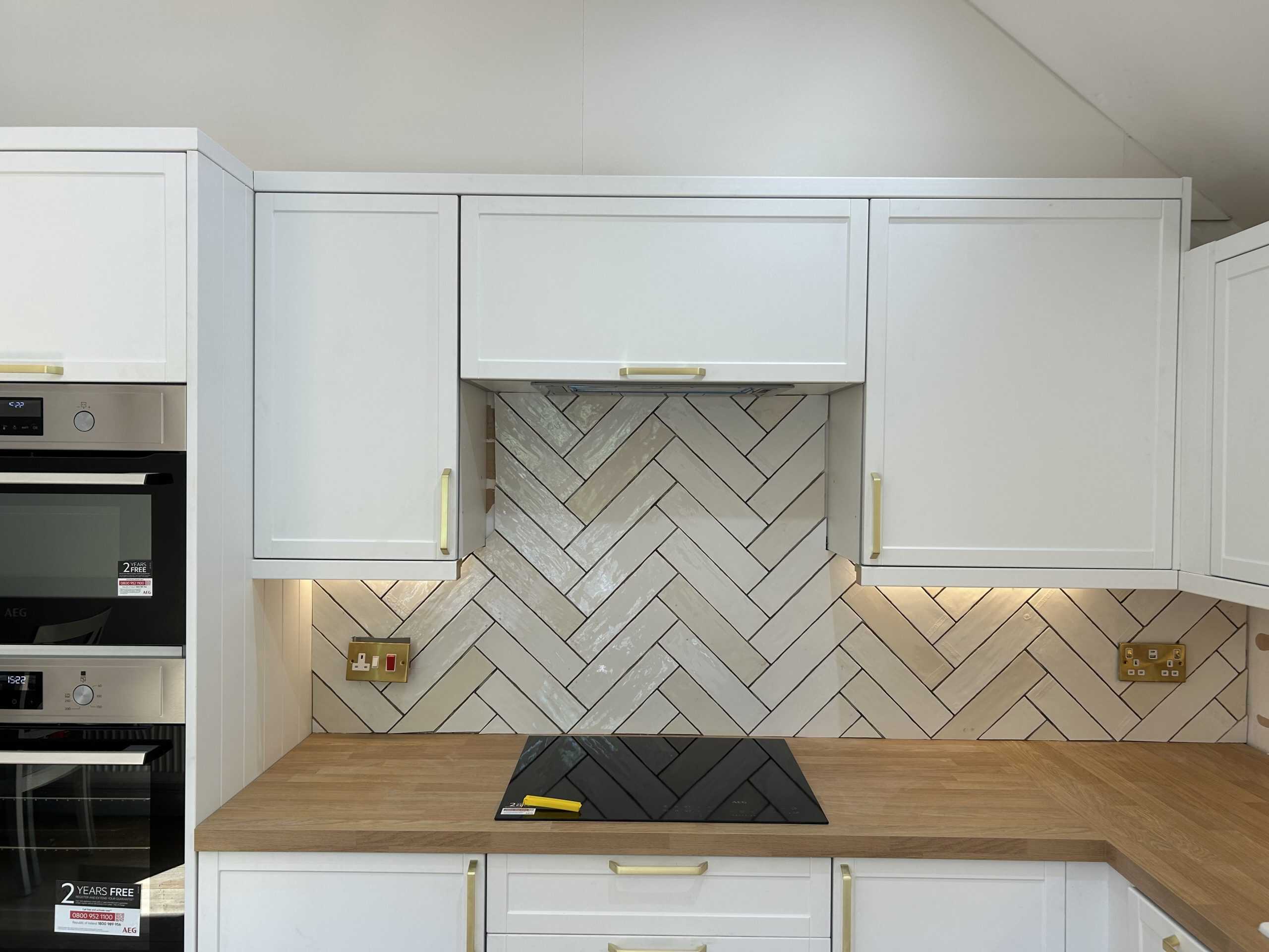 Modern white kitchen cabinets with a wooden countertop and herringbone backsplash.