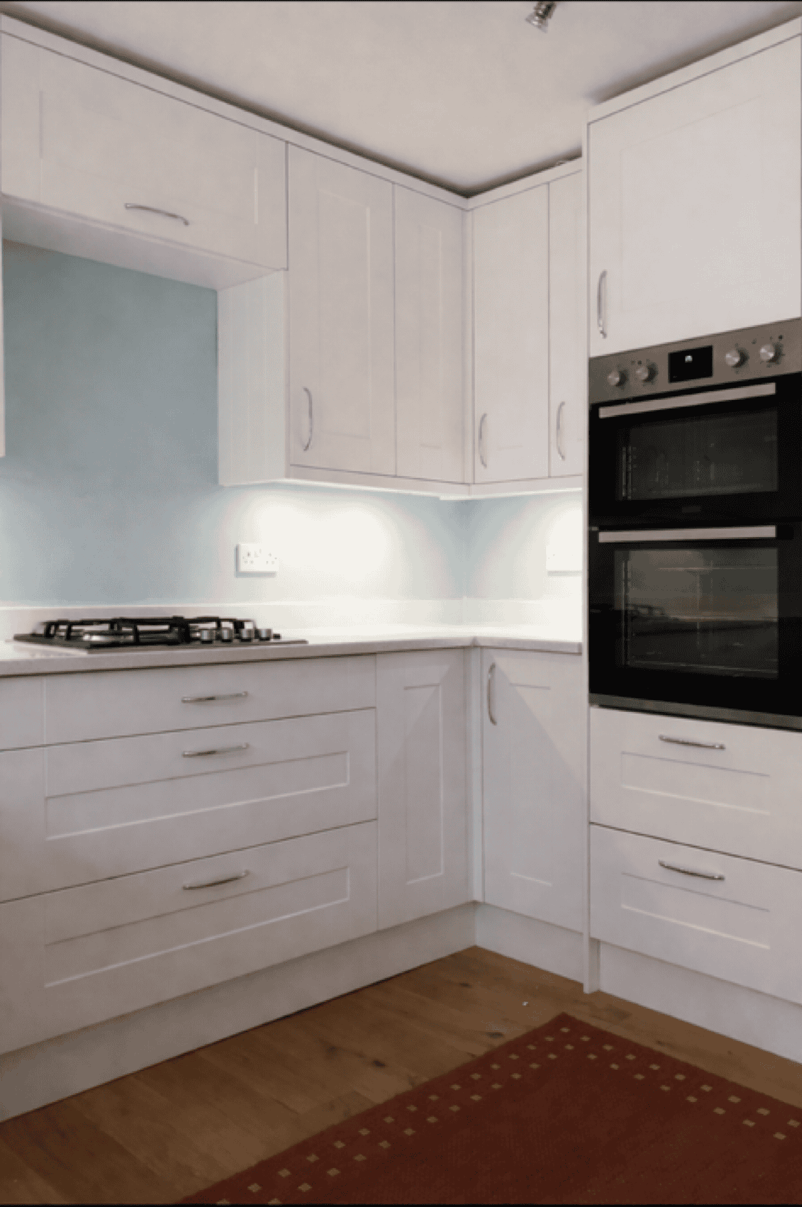 Modern white kitchen with built-in oven and stove.