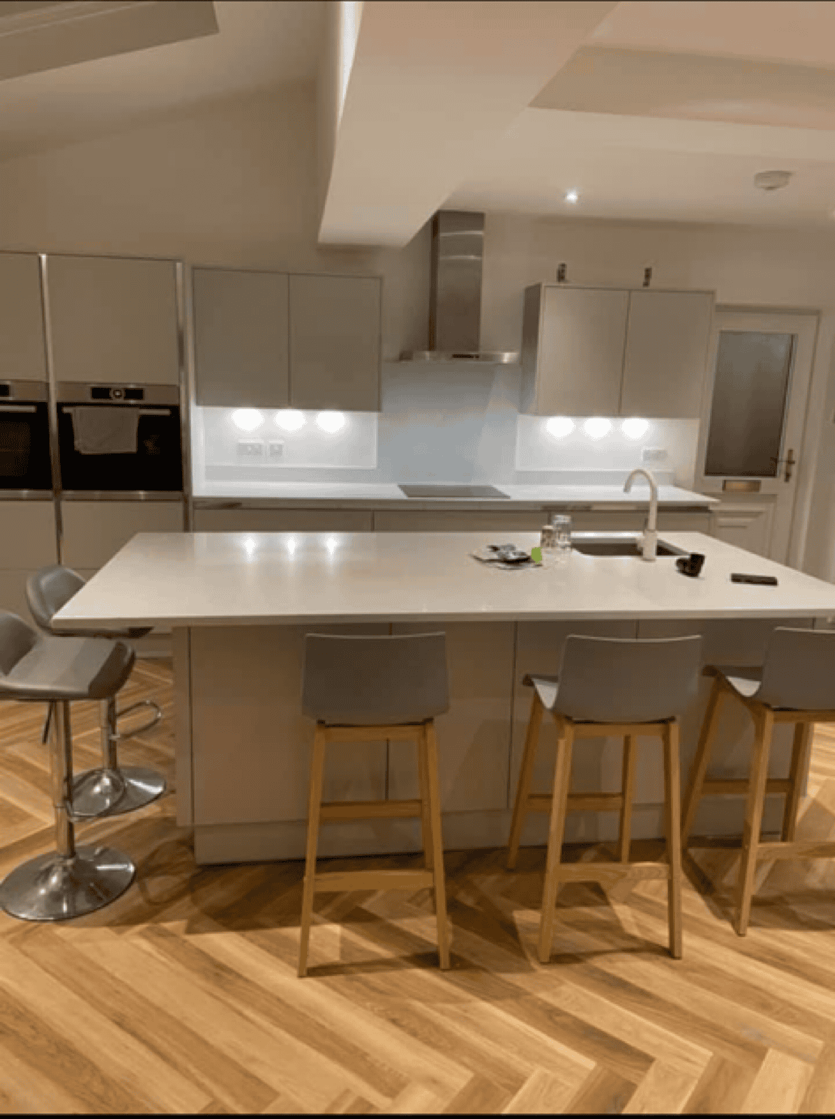 Kitchen with white cabinets, wooden flooring, and a central island with bar stools, showcasing a sle.