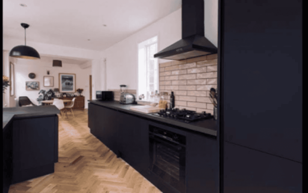 Black kitchen cabinets with built-in oven and stove, brick backsplash, and open-plan living area in.