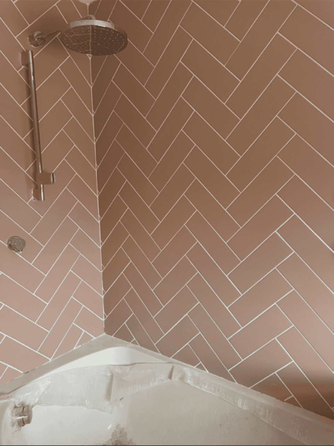 Herringbone tiled shower wall with rainfall showerhead in a bathroom renovation.