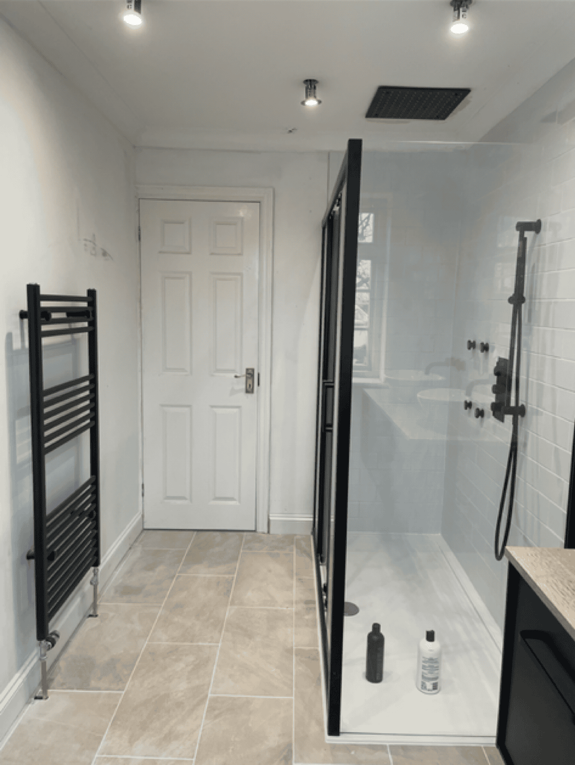 Walk-in shower with glass door and black fixtures in a contemporary bathroom.