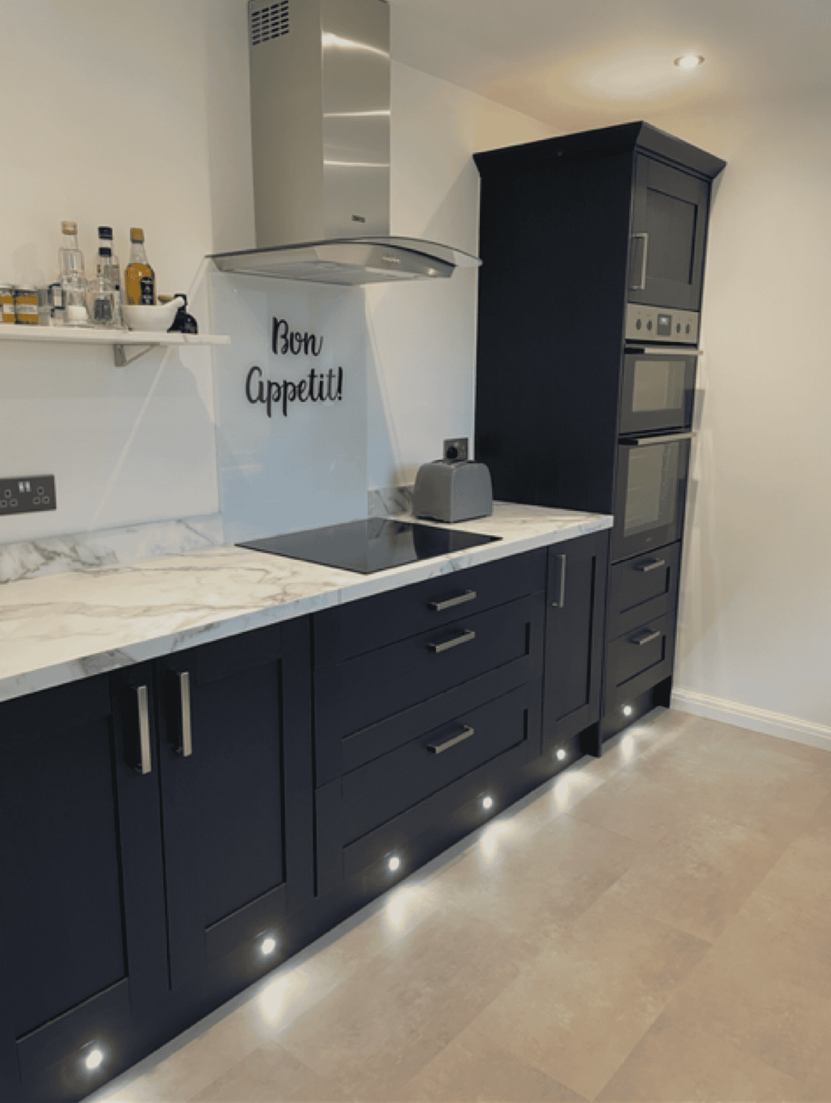 Navy kitchen cabinets with built-in oven, microwave, and modern extractor fan. Under-cabinet lightin.