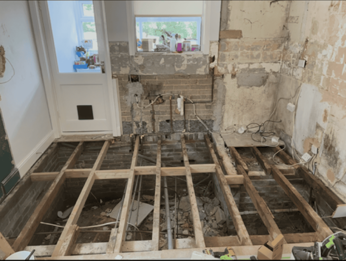 Kitchen floor renovation with exposed wooden joists and construction materials.