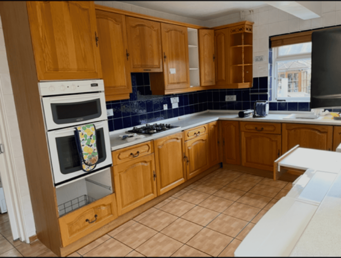 Kitchen cabinetry installation with wooden units and black tiled backsplash.