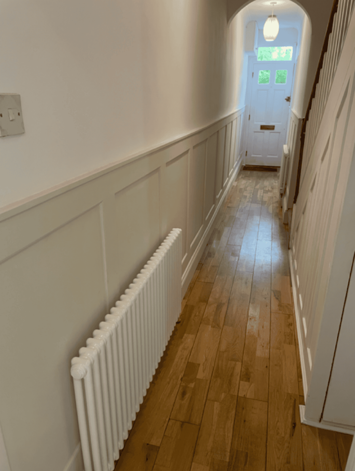 Hallway with wooden flooring, white wall paneling, and a radiator near the wall.