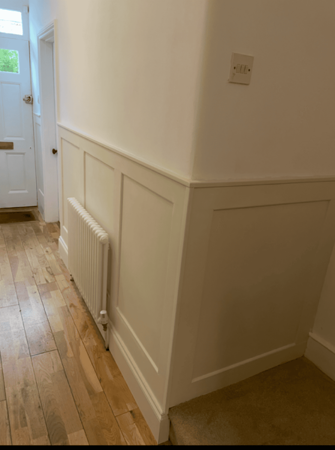Radiator and wall paneling in a hallway corner.